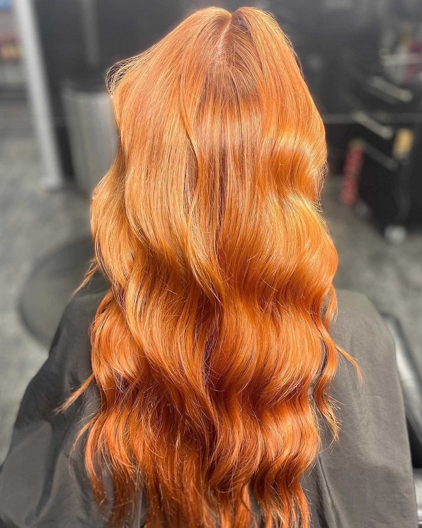 Long, wavy red-orange hair styled elegantly in a salon.