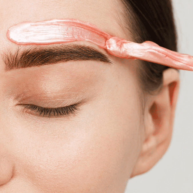 Eyebrow waxing application with a spatula and pink wax on a closed eye.